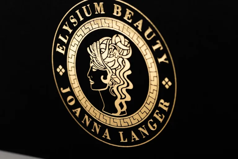 Złote logo Elysium Beauty na czarnej powierzchni
