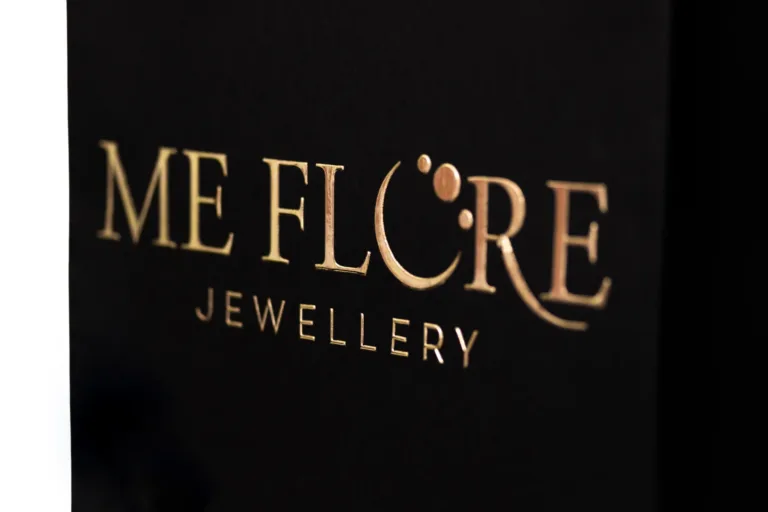 Złote wypukłe logo Me Flore Jewellery na czarnym tle